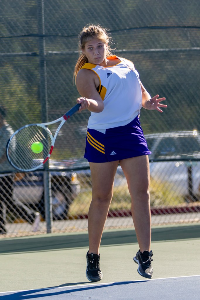 A female tennis player in action on the court, preparing to hit a tennis ball while wearing a sports outfit.