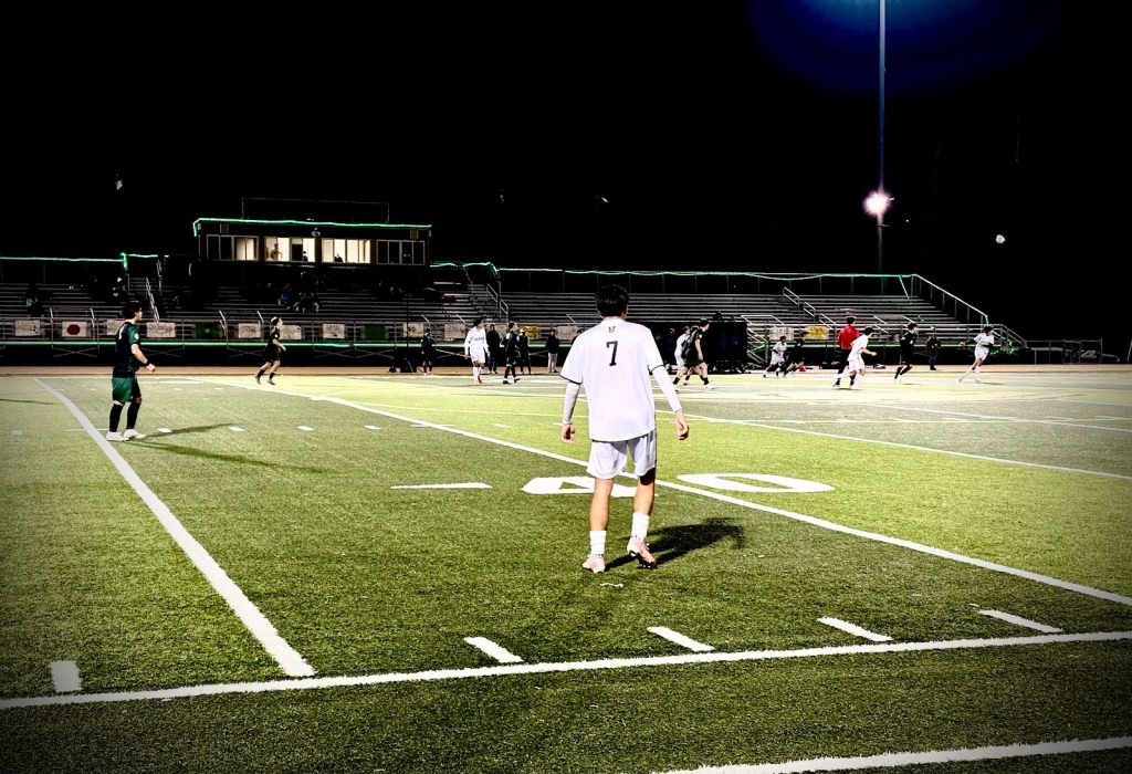 A soccer match taking place at night, with players in action on a well-lit field. The focus is on a player wearing a white jersey with the number 7, while other players are positioned in the background.